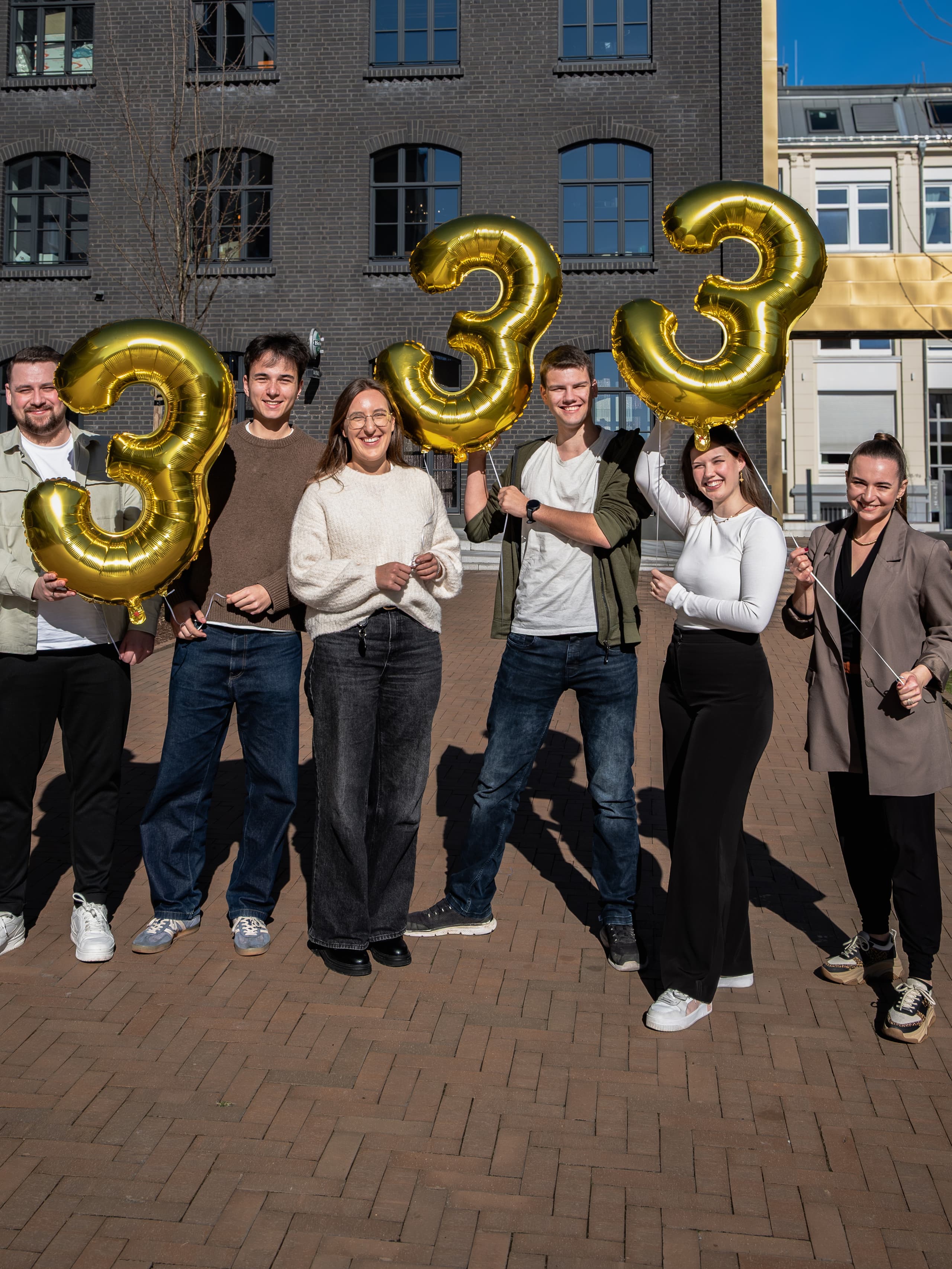 MUUUH!-Team feiert einen Meilenstein mit goldenen 333-Zahlenballons vor dem Büro