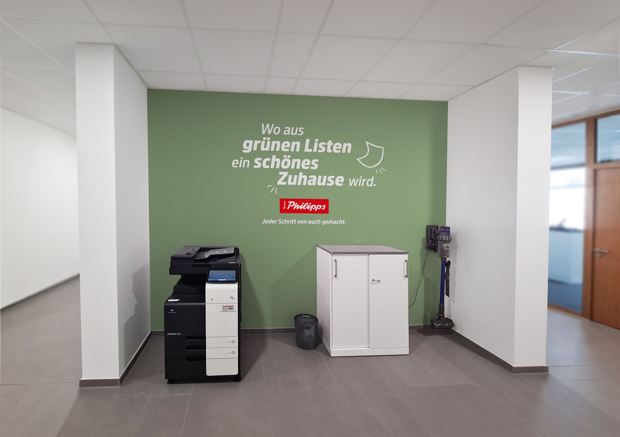 Moderne Büroumgebung bei Thomas Philipps mit grüner Markenwand und Kopierstation