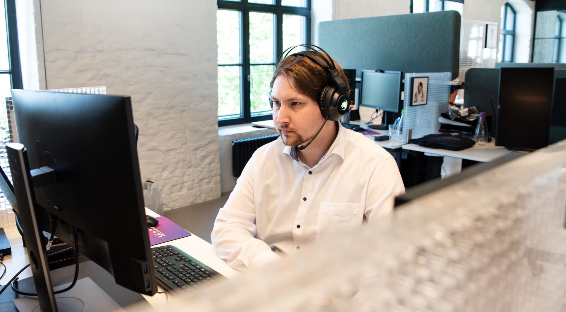 Alexander Schmidt, Expert Customer Experience Agent bei MUUUH!, bei der Arbeit am Computer mit Headset