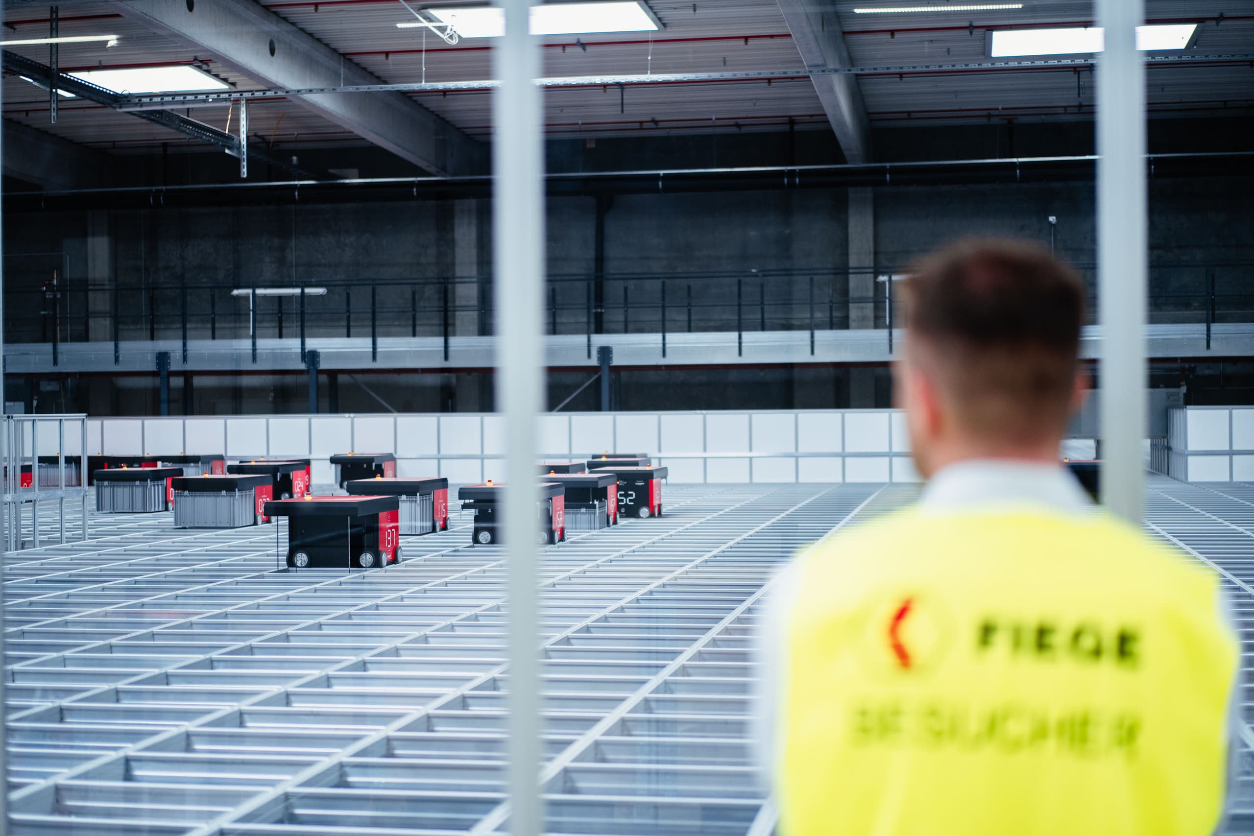 Person in FIEGE-Weste blickt in moderne Logistikhalle mit markierten Bodenflächen