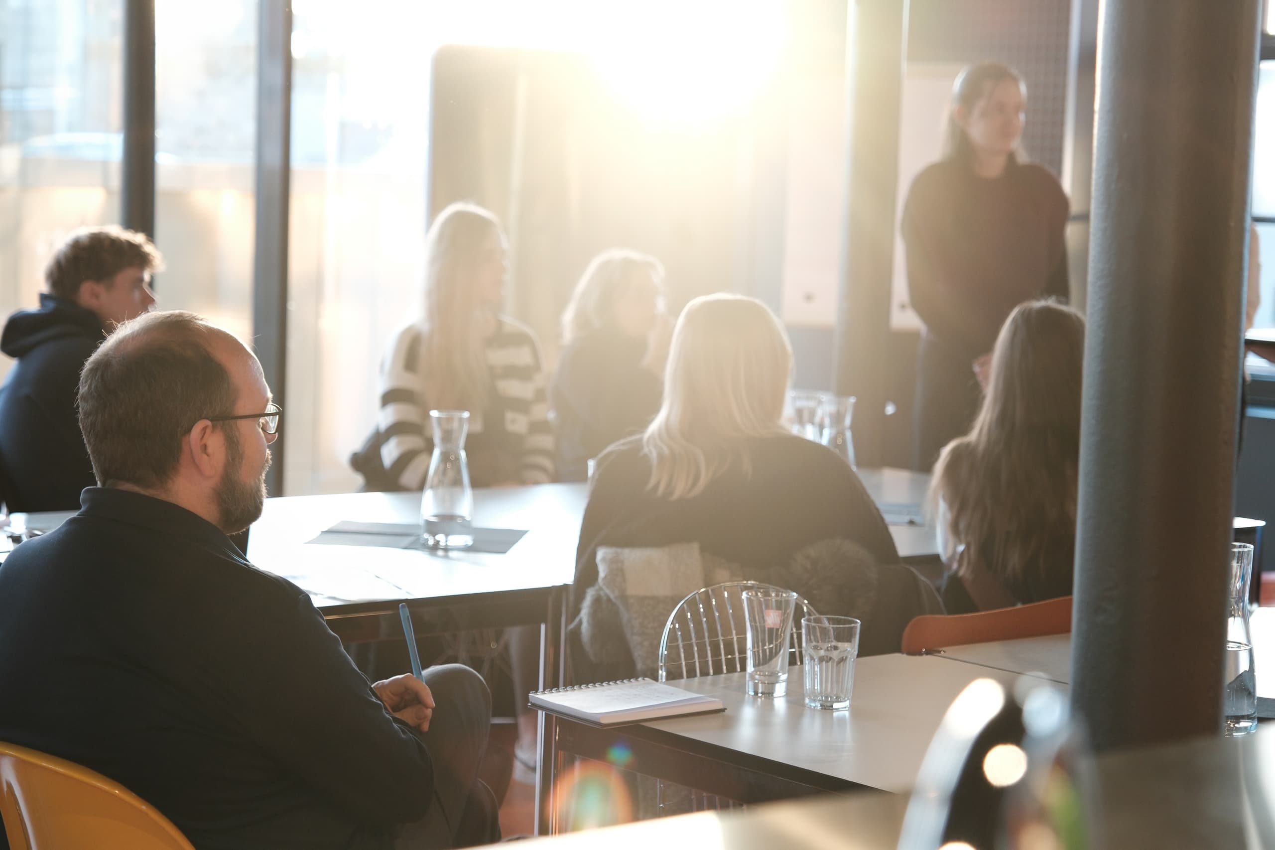 Teilnehmende sitzen in einem Workshop-Raum, eine Person prasentiert vor der Gruppe im Gegenlicht