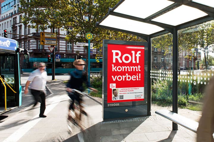 Citylight-Plakat 'Rolf kommt vorbei!' an einer Bushaltestelle in Osnabrueck – SWO-Kampagnenmotiv im Stadtbild