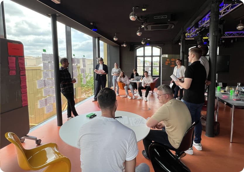 Workshop-Session mit Teilnehmenden: Eine Person praesentiert Ergebnisse an einer Glaswand mit Post-its