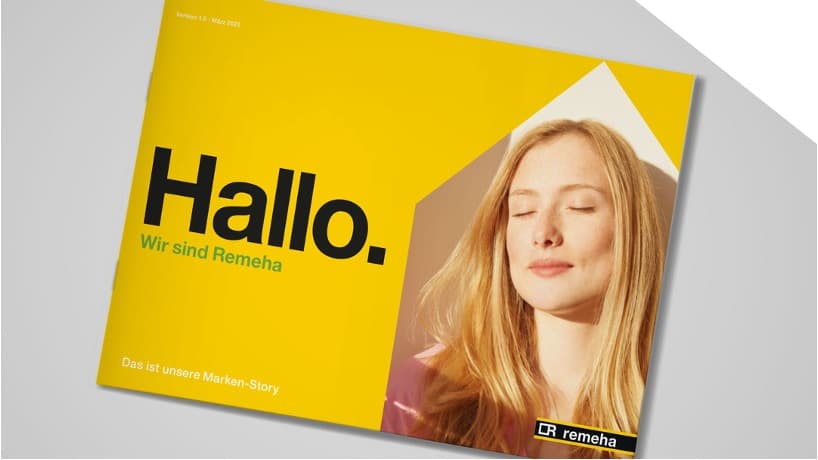Aufgeschlagener Remeha Brand Guide mit gelbem Cover: 'Hallo. Wir sind Remeha – Das ist unsere Marken-Story'