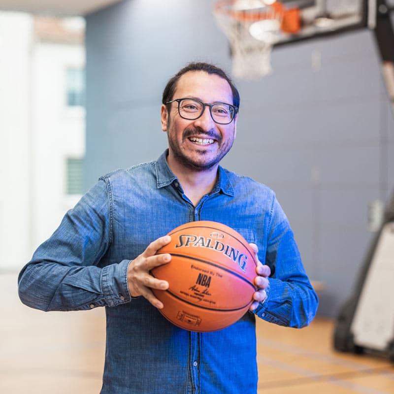 Patricio Zaun, Teamleiter bei MUUUH!, lächelt in die Kamera und hält einen Basketball in einer Sporthalle