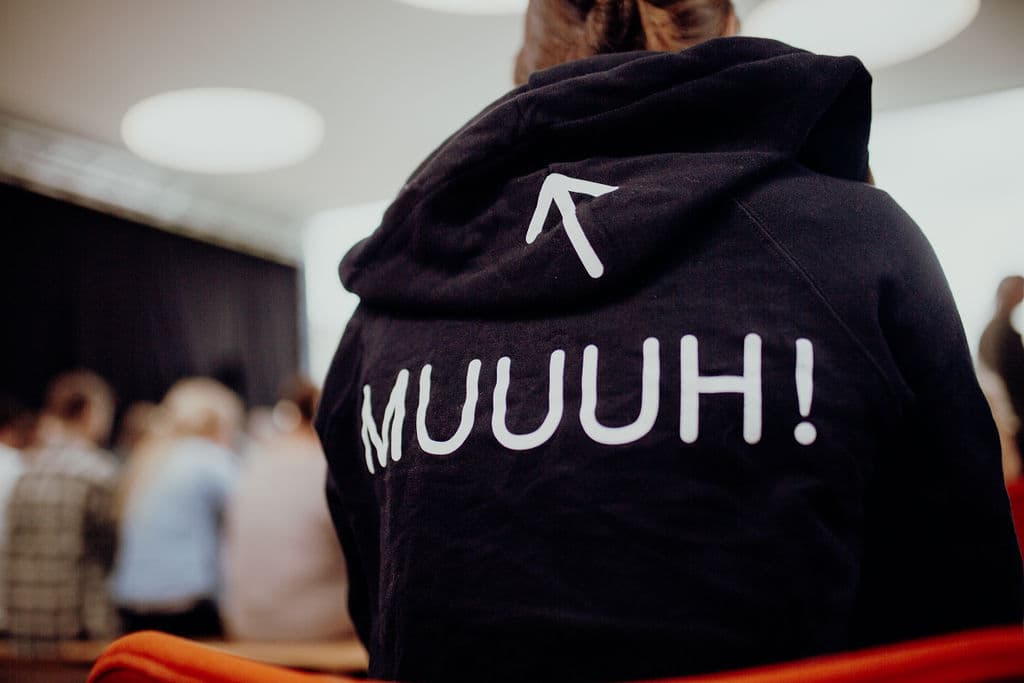 Person von hinten trägt schwarzen Hoodie mit weißem Pfeil und Schriftzug 'MUUUH!' auf dem Rücken