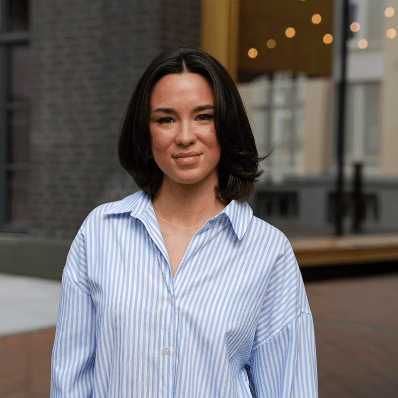 Leoni Hock, Advanced Consultant bei MUUUH!, lächelt in die Kamera vor einem urbanen Hintergrund