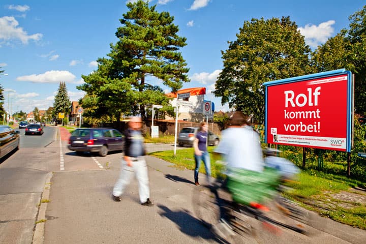 Großflächenplakat der SWO-Kampagne mit der Aufschrift 'Rolf kommt vorbei!' an einer Straße in Osnabrück