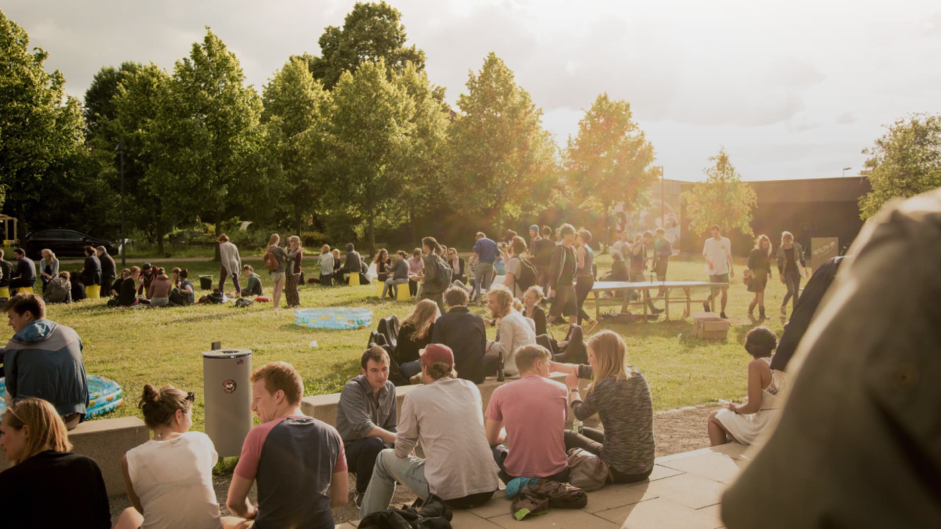 Studierende der FH Münster sitzen und stehen im Freien auf dem Campus bei warmem Abendlicht