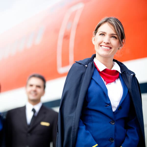 Lächelnde Flugbegleiterin in blauer Uniform mit rotem Tuch vor einem Flugzeug – GVO-Recruiting-Kampagne