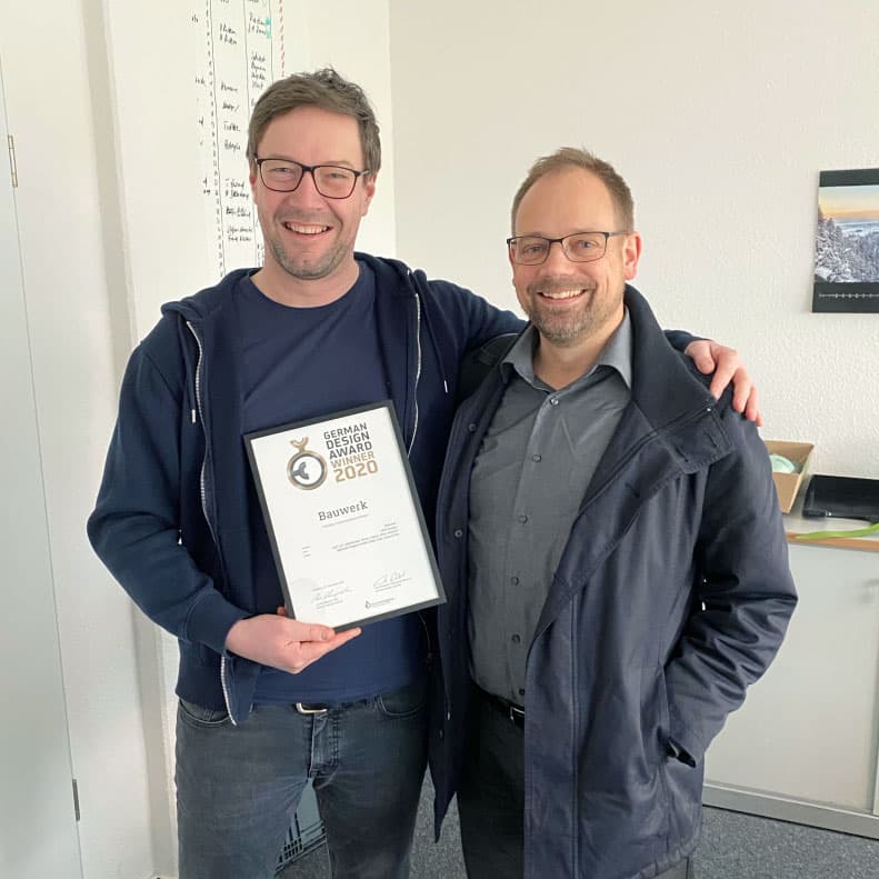 Dirk Kolhosser, Executive Creative Director bei MUUUH!, hält mit einem Kollegen die German Design Award 2020 Auszeichnung für das Bauwerk-Magazin