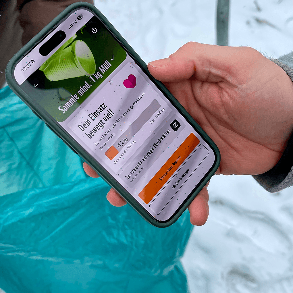 Hand hält Smartphone mit PandAktiv-App: Challenge 'Sammle mindestens 1 kg Müll' und Fortschrittsanzeige im Freien