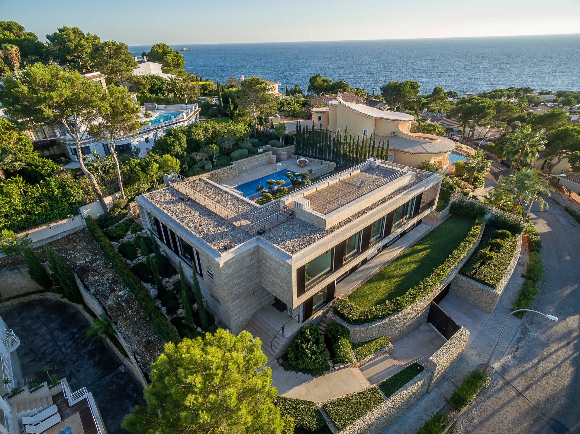 Luftaufnahme einer modernen Luxusvilla auf Mallorca mit Pool auf der Dachterrasse, umgeben von mediterraner Vegetation und Meerblick
