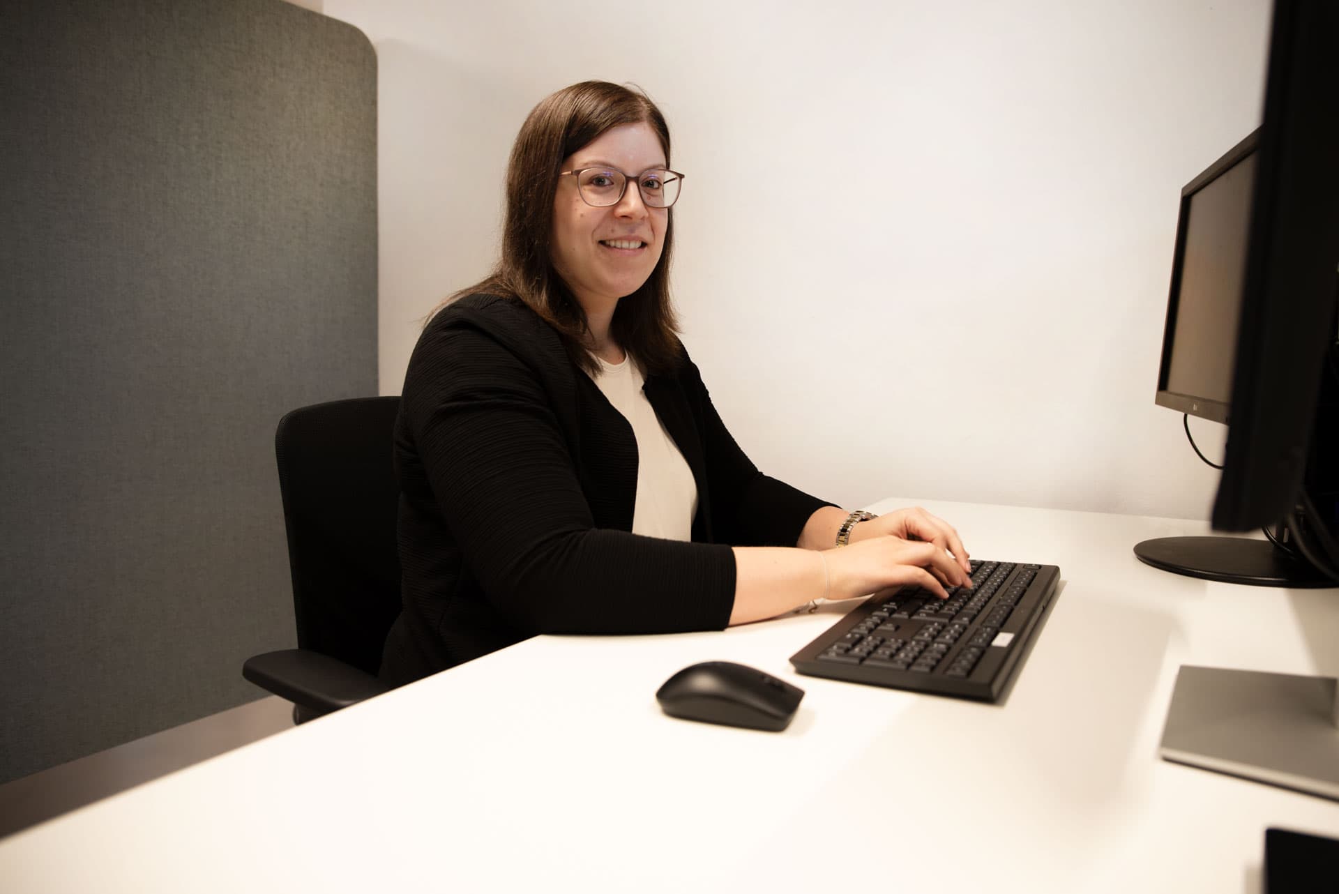 Vanessa Holler lächelt am Schreibtisch mit Tastatur und Monitor in einem modernen Büroarbeitsplatz