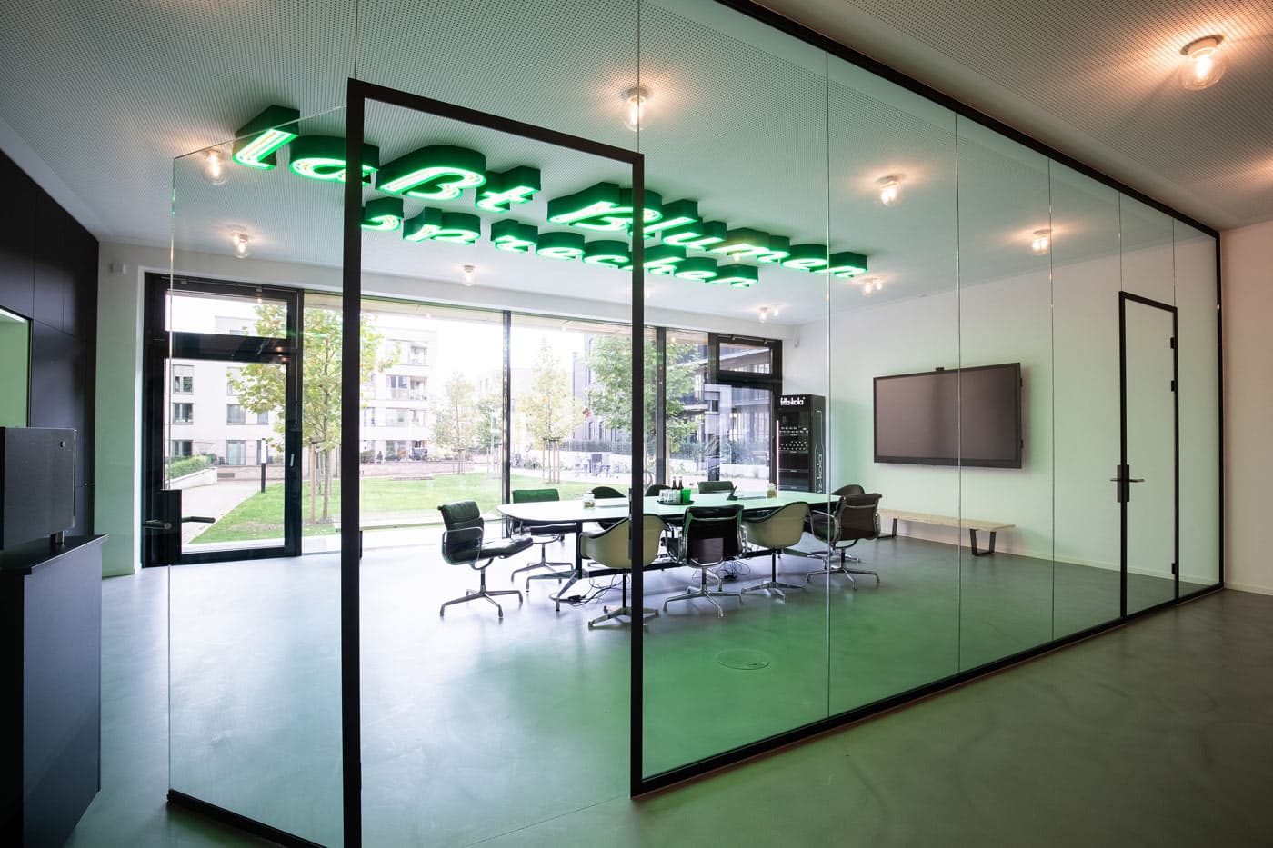 Moderner Konferenzraum im Hageloft mit Glaswänden, grüner Neon-Deckeninstallation und Blick ins Freie