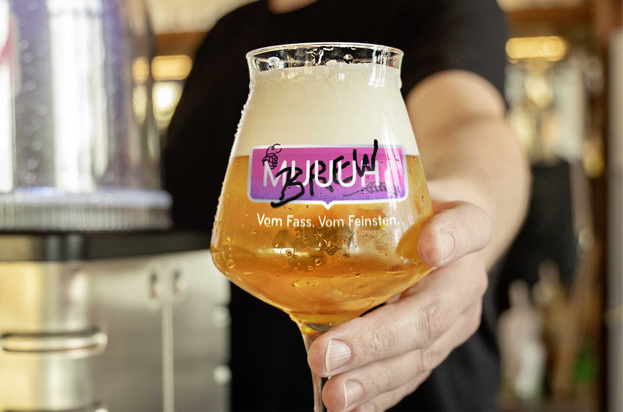 Hand hält ein Craft-Beer-Glas mit MUUUH! Brew-Logo und dem Schriftzug 'Vom Fass. Vom Feinsten.'