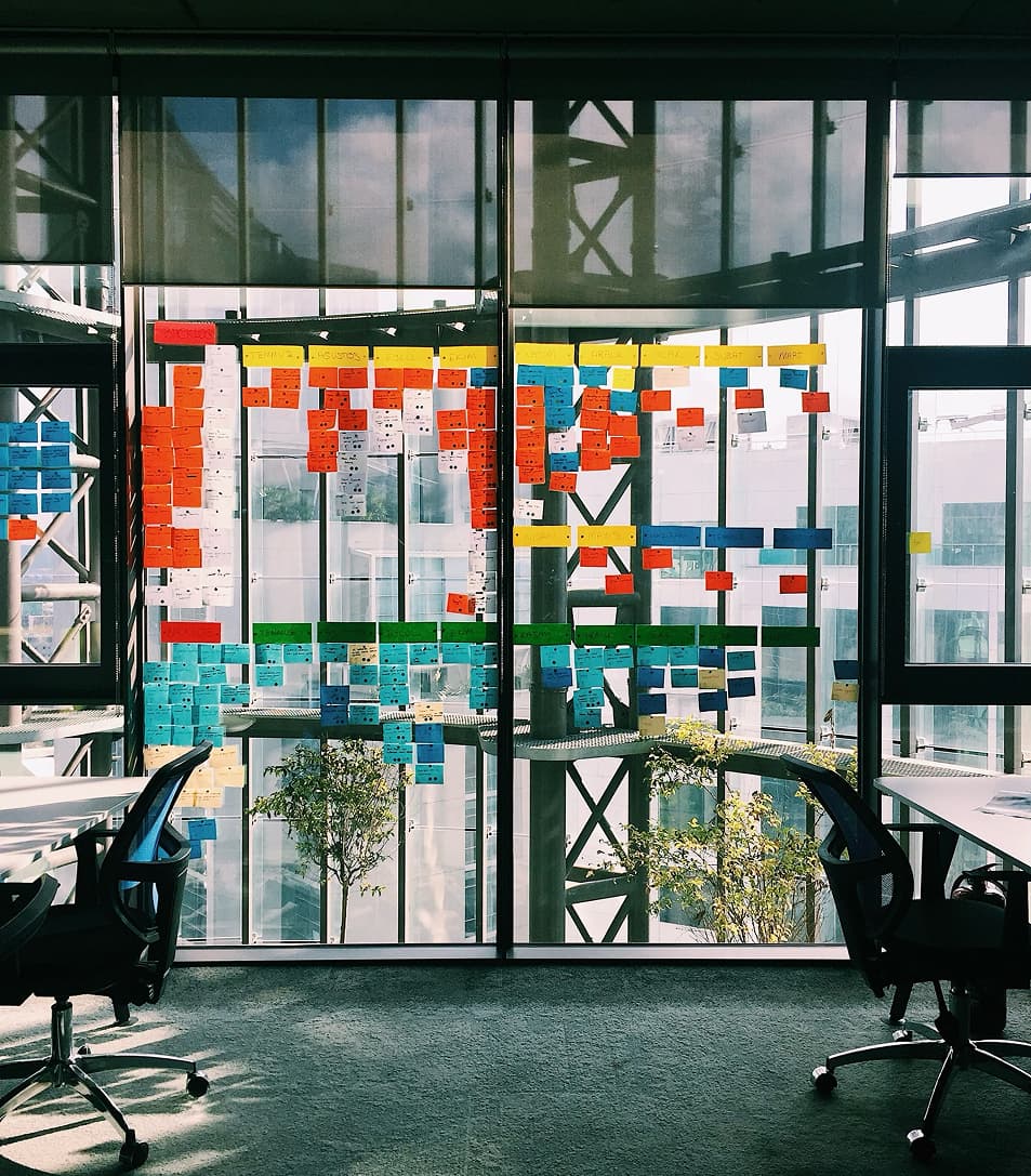 Großes Glasfenster in einem Büro, übersät mit bunten Post-its in einem strukturierten Muster — symbolisch für datenbasierte Marketingplanung
