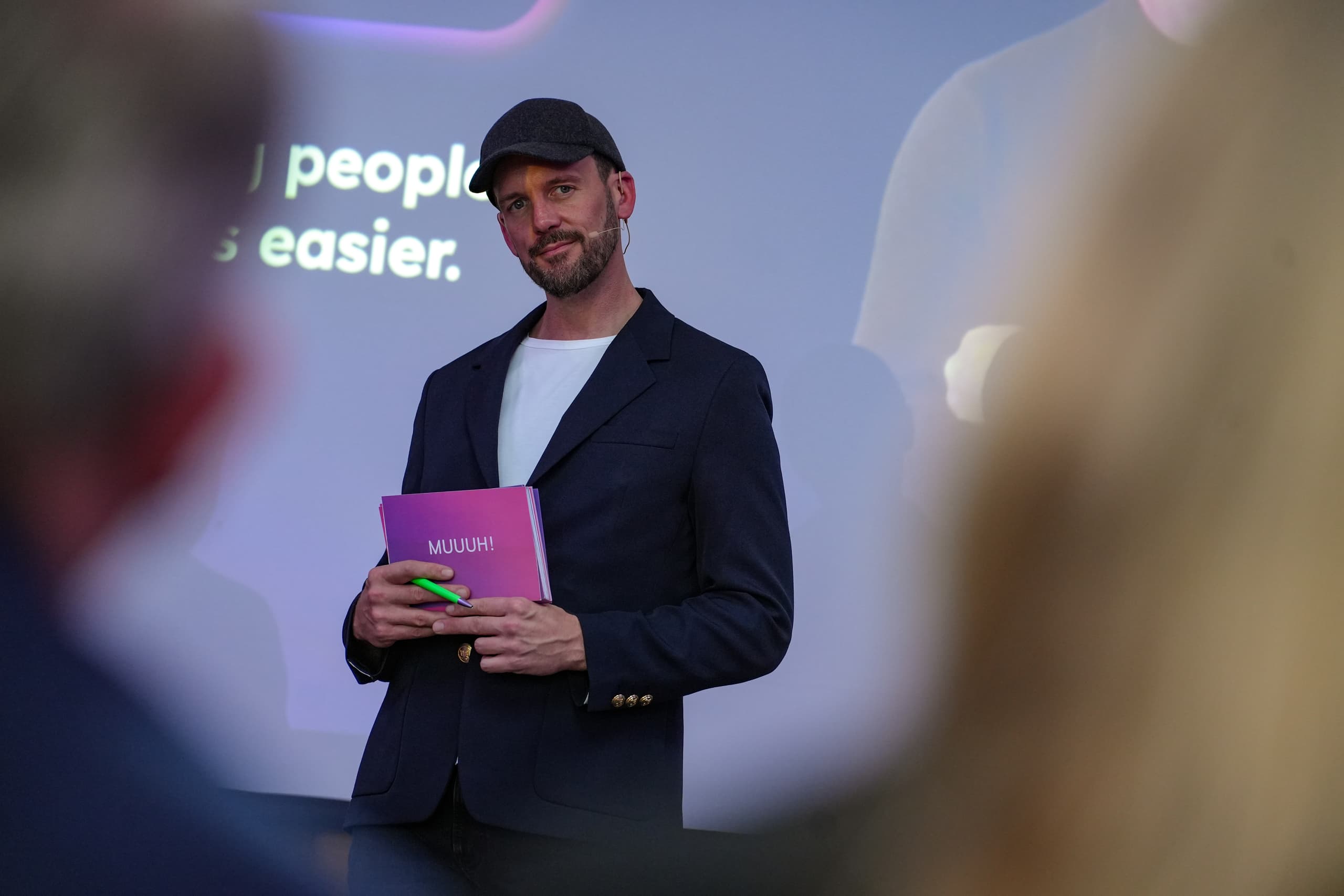 Moderator mit MUUUH!-Mappe präsentiert auf der MUUUHnwalk-Veranstaltung zum Thema Future of Customer Care