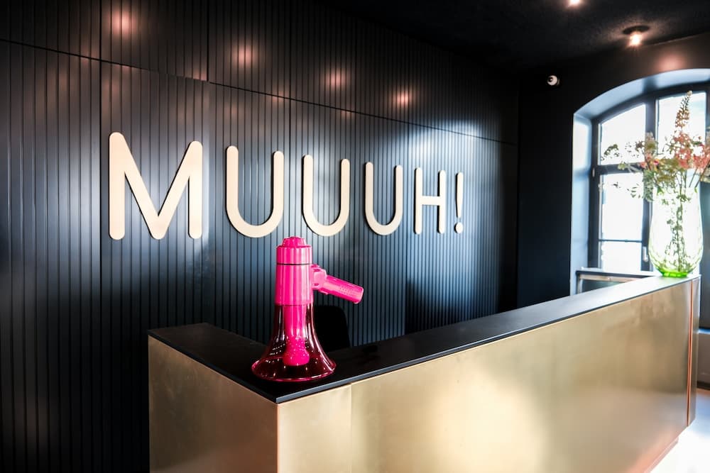 Empfangstheke im MUUUH!-Büro mit leuchtendem Schriftzug 'MUUUH!' an der Wand und pinkfarbenem Megafon