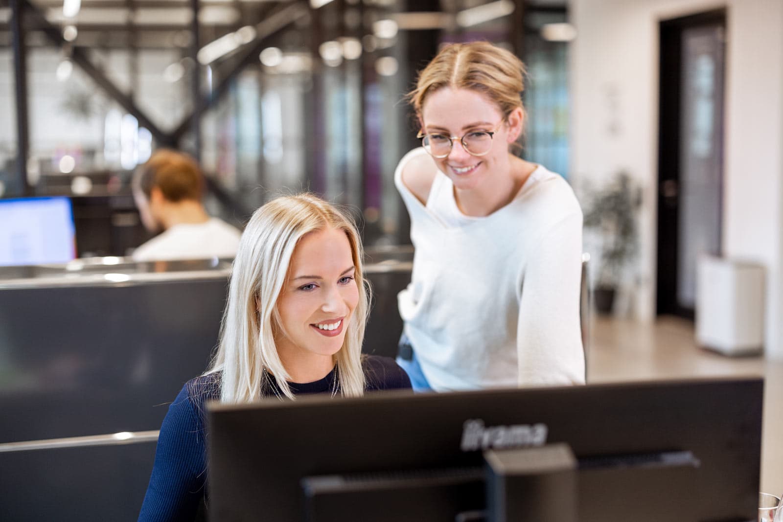 Inga und Kollegin arbeiten gemeinsam an einem PC-Monitor in einem modernen Büro bei Hageloft