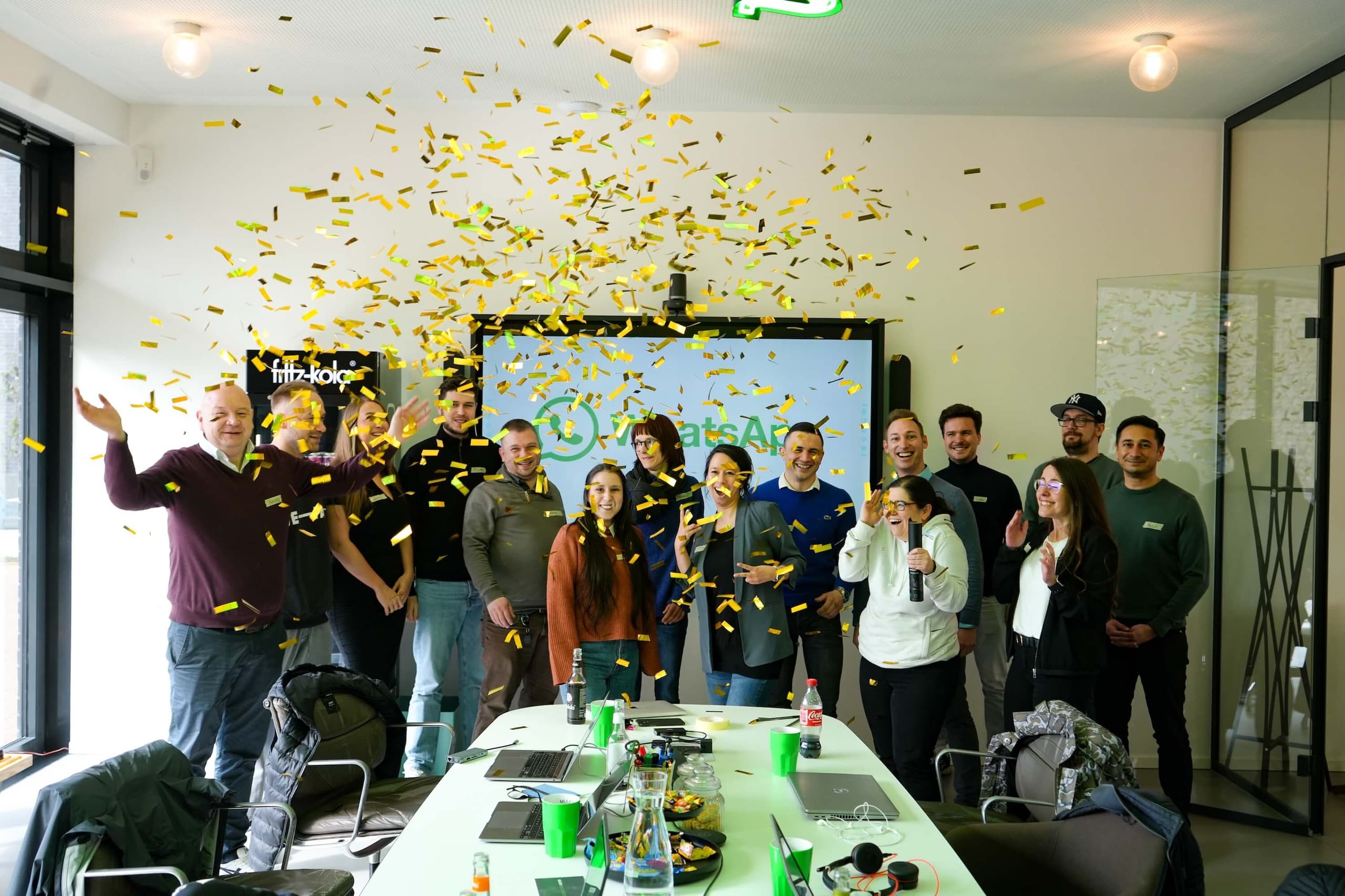 Team feiert den WhatsApp-Launch von Deutsche Glasfaser und MUUUH! mit goldenem Konfettiregen im Besprechungsraum