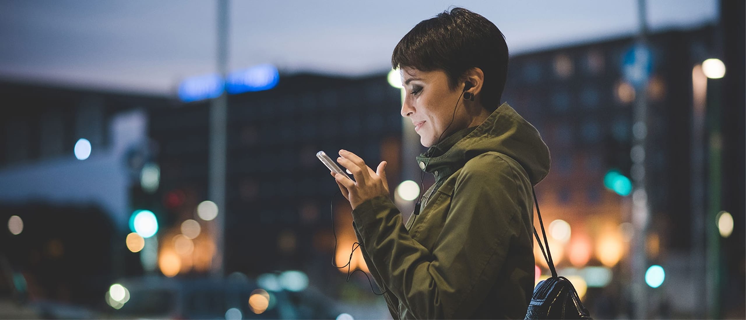 Frau schaut auf ihr Smartphone in nächtlicher urbaner Umgebung