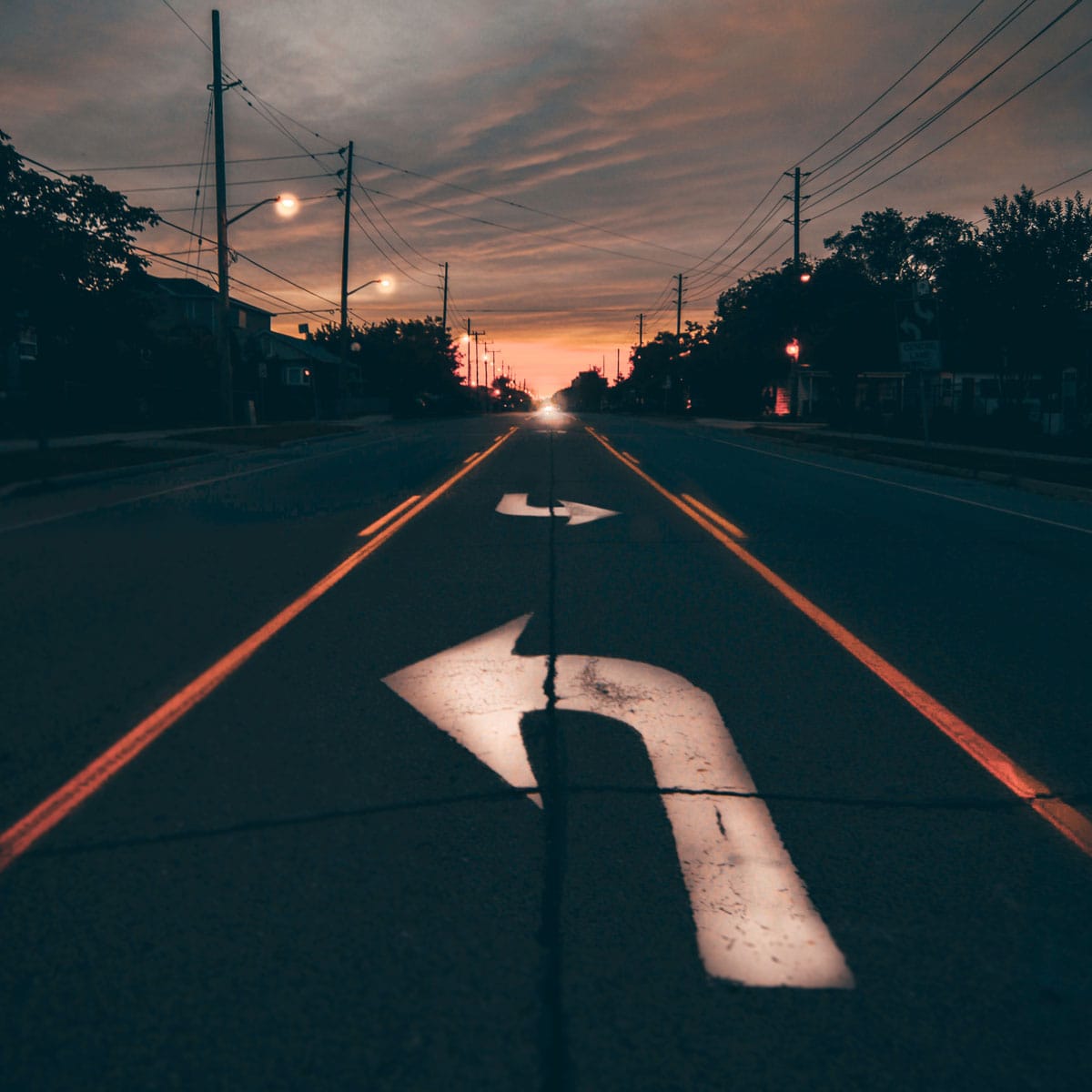 Richtungspfeile auf einer Straße bei Sonnenuntergang als Metapher für Reorganisation und Neuausrichtung