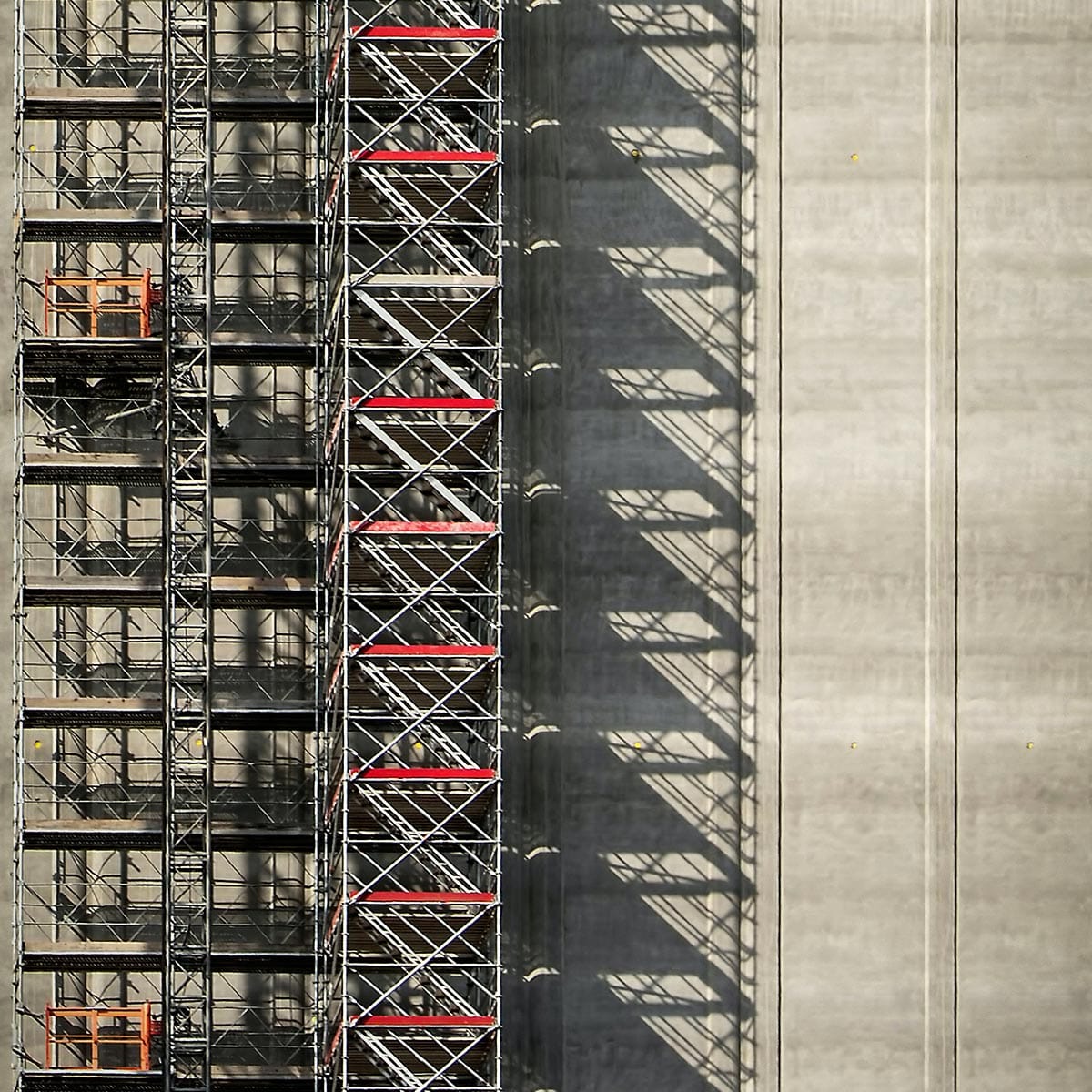 Metallgerüst mit roten Querstreben wirft geometrische Schatten auf eine Betonwand – Symbol für Digitalisierung in der Baubranche