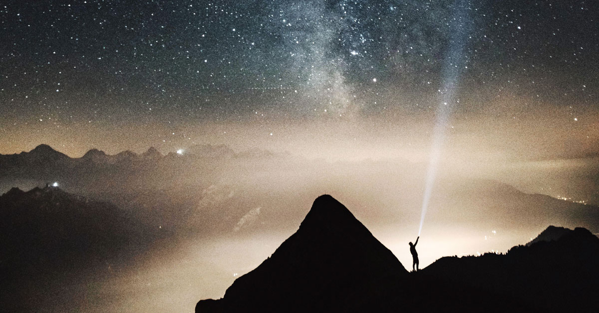 Mann auf Berg unter Sternenhimmel mit Taschenlampe