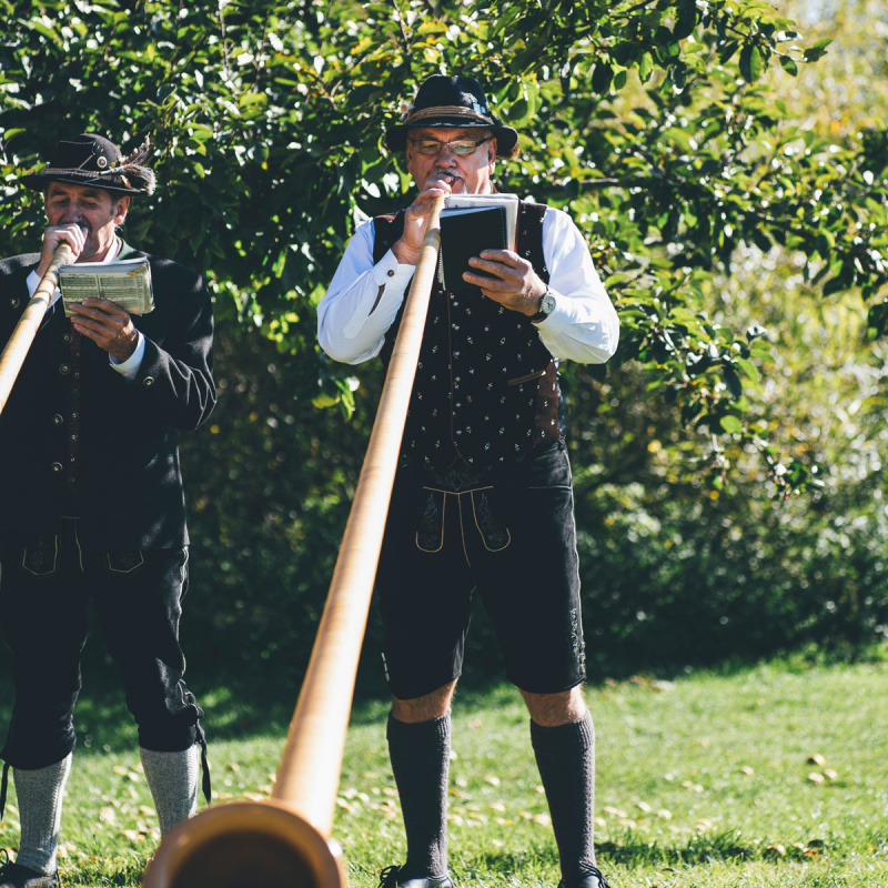 Zwei Männer spielen auf einem Alphorn in Tracht 