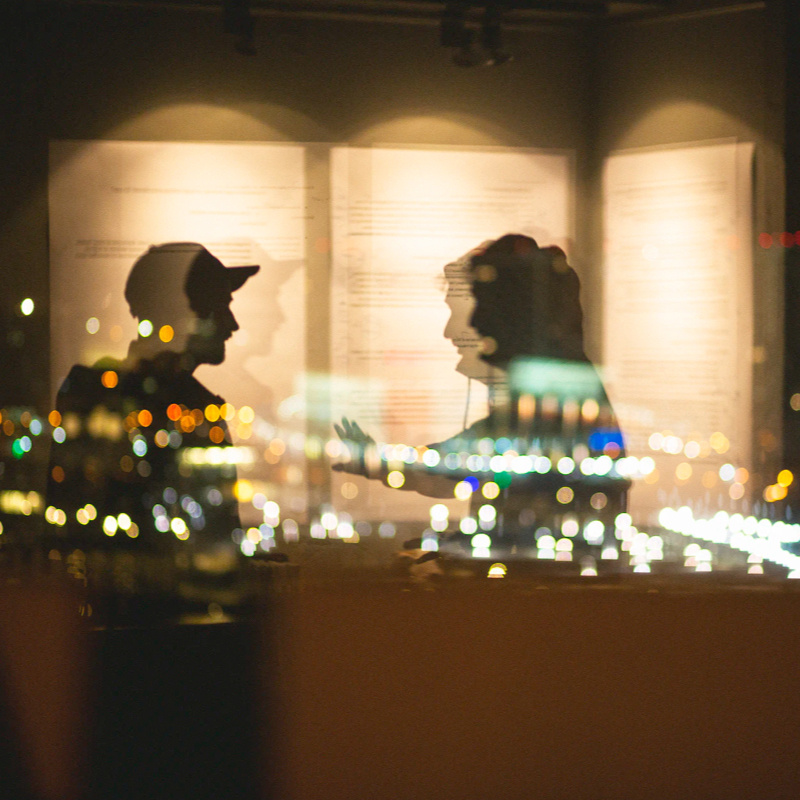 Lichter und Silhouette von zwei Personen spiegeln sich in einem Fenster