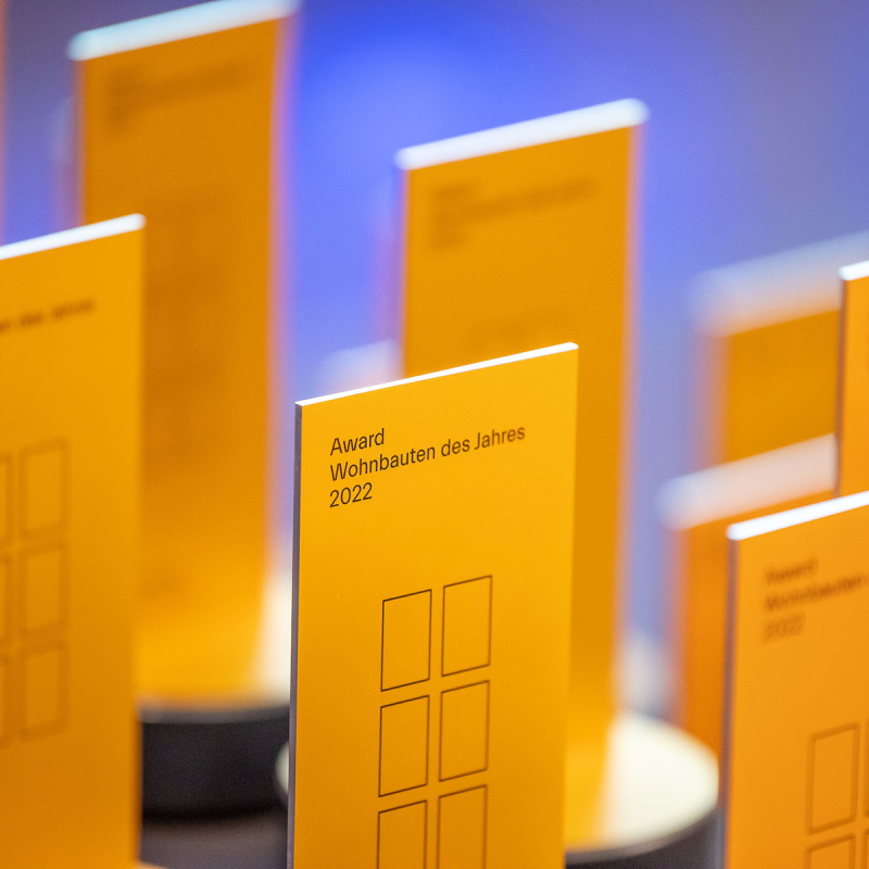 Mehrere goldene Trophäen mit dem Titel "Award Wohnbautes des Jahres 2022" stehen auf einem Tisch.