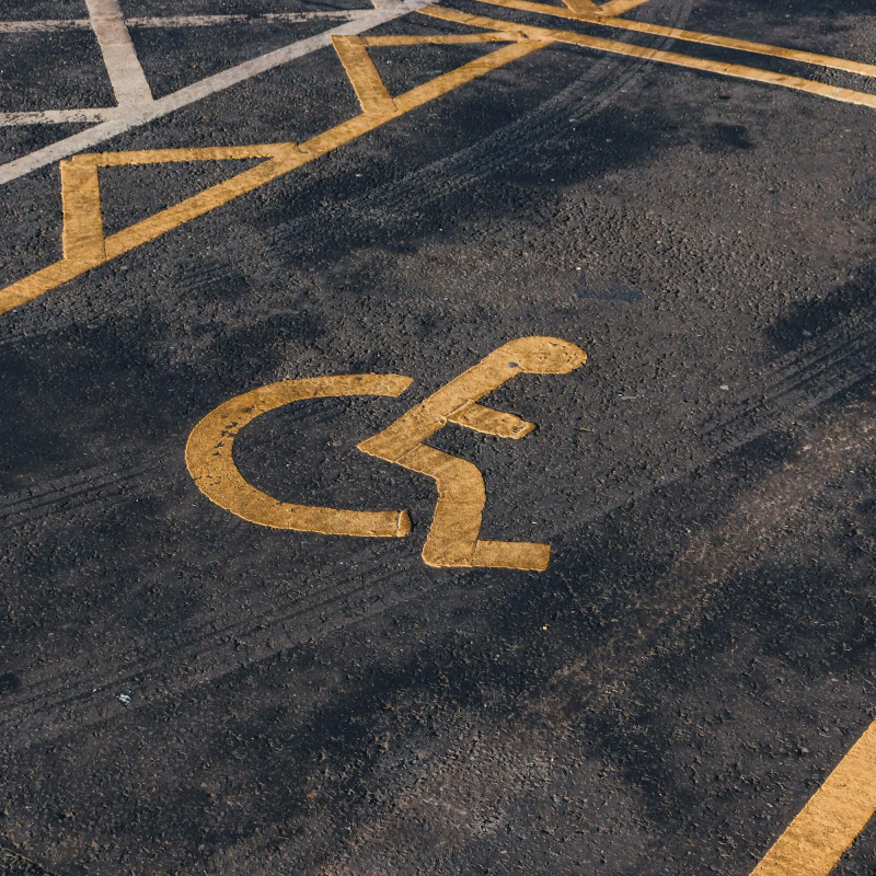 Behindertenparkplatz mit gelber Darstellung eines Rollstuhls mit Person auf Asphalt
