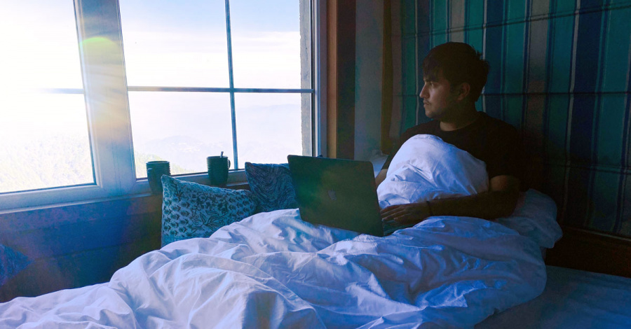 Mann mit Laptop im Bett schaut aus dem Fenster