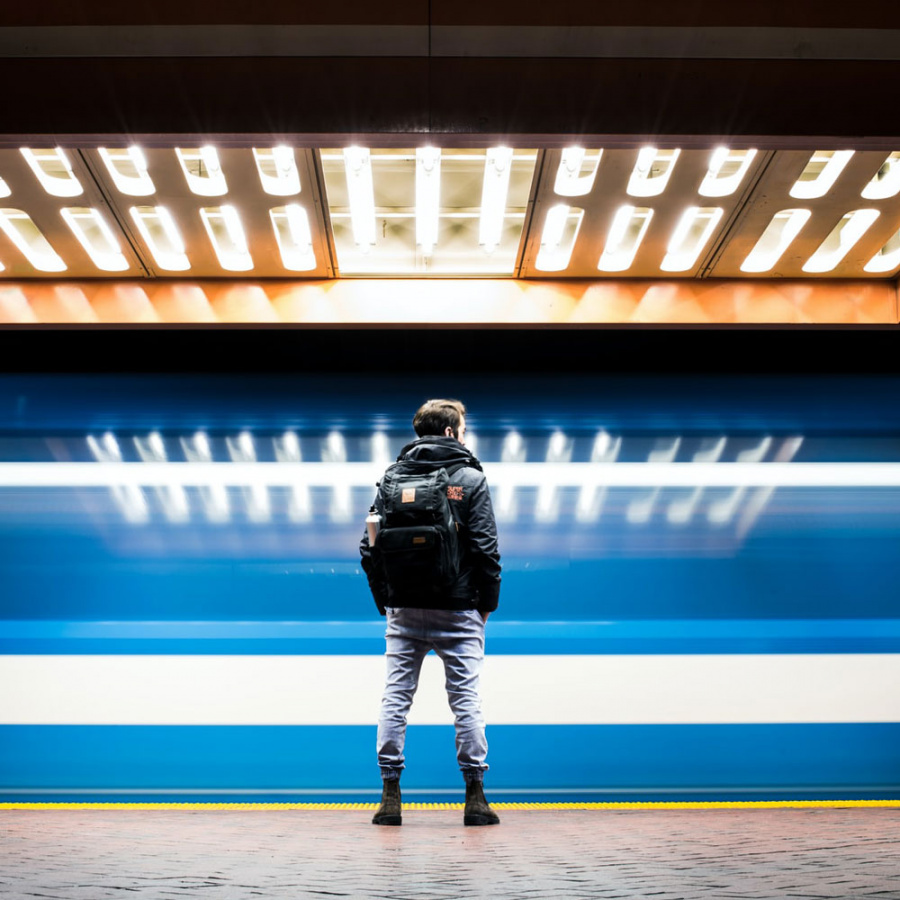 Junger Mann steht am Bahnsteig vor vorbeifahrendem Zug