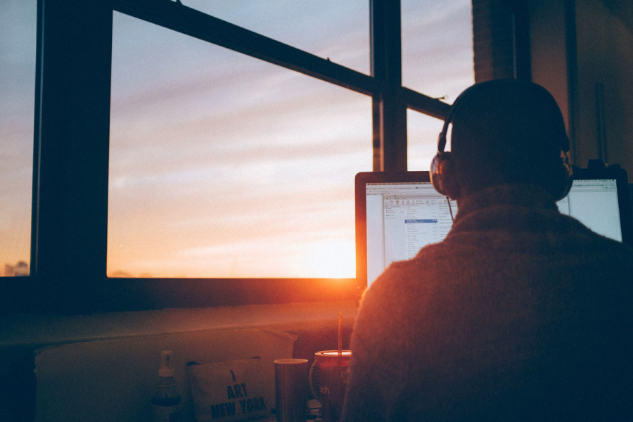 Mann sitzt vor PC, im Hintergrund geht die Sonne unter