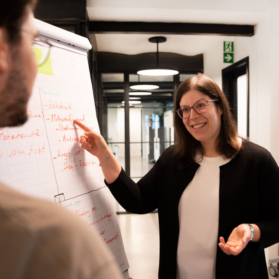 Mitarbeiterin Vanessa Holler von MUUUH! Dialogue erklärt einem Kollegen etwas vor einem Flipchart